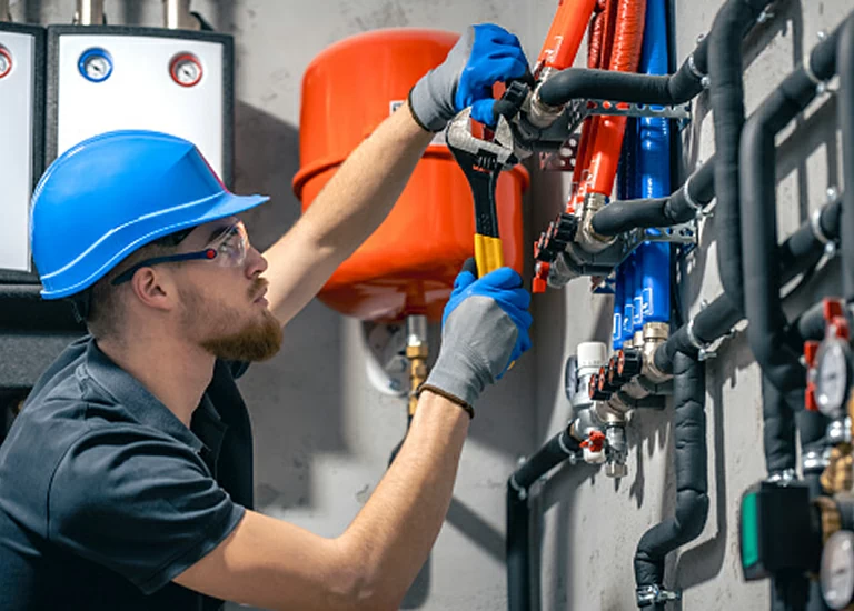 Technician in blue hard hat and safety glasses tightening pipes on industrial equipment