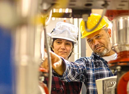 Two workers in hard hats inspecting industrial equipment on a factory floor